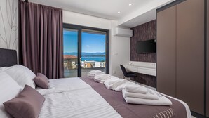 A modern hotel room with a large bed, a desk, a TV, and a view of the sea.