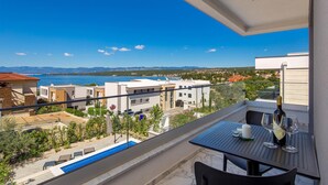 A balcony with a pool, a table with a bottle and glasses, and a view of the sea and buildings.