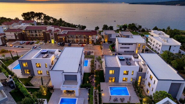 A modern hotel complex with multiple buildings, rooftop pools, and a view of a lake at sunset.