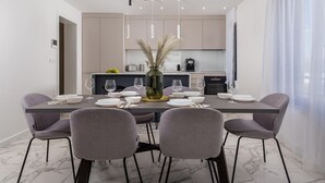 A modern dining area with a marble-tiled floor, grey upholstered chairs, a central table set for four, and pendant lighting.
