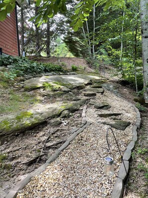 A garden pathway with a wooden bench, surrounded by rocks and pebbles, leading to a house. - Spacious garage apartment with views of Pisgah Mountain and Blue Ridge Mountains (Brevard)