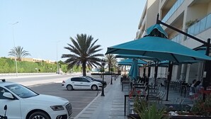 Une vue de rue avec un café doté d’une terrasse, une voiture blanche et une moto garée sur le côté.