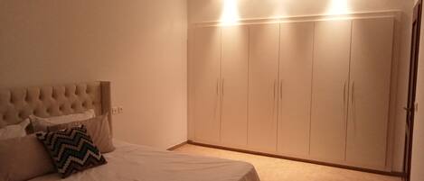 A bedroom with a bed, a headboard, a wardrobe, and a carpeted floor.