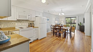 Una cocina moderna con armarios blancos, horno empotrado y comedor con sillas y mesa de madera.