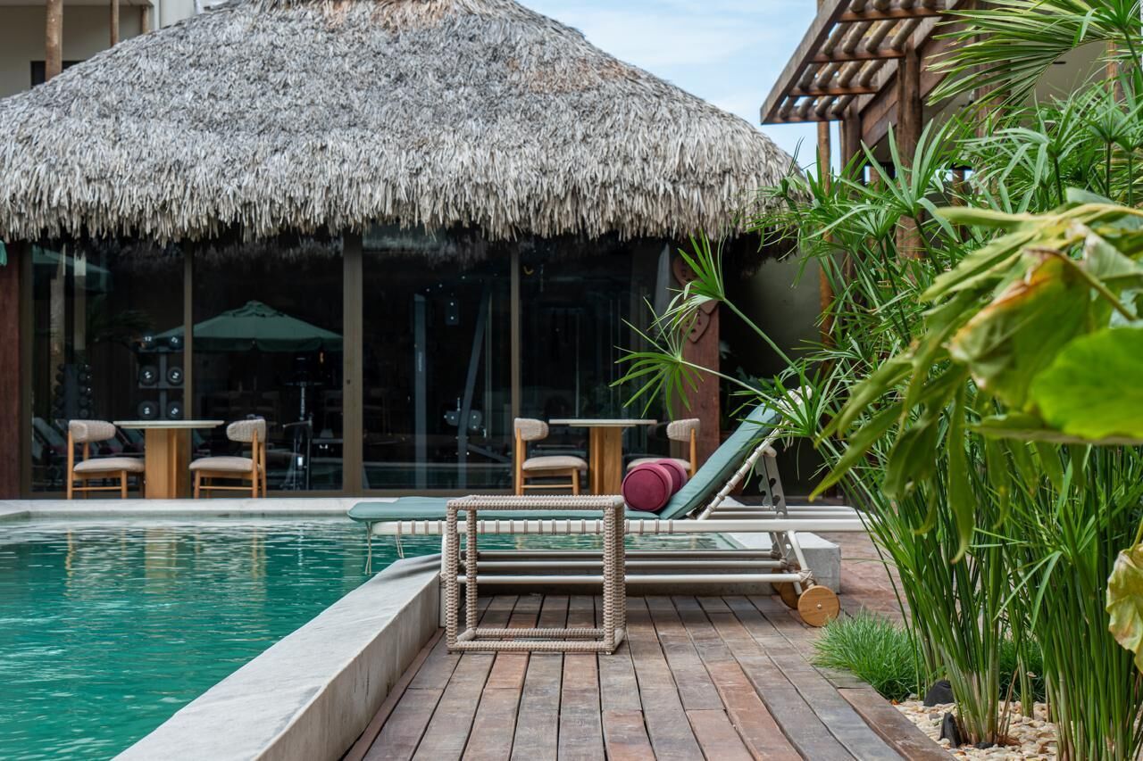 A pool area with a thatched roof structure, lounge chairs, and a small table.