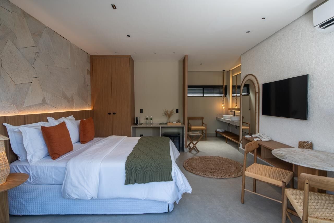 A modern hotel room with a large bed, a desk, a chair, a TV, and a mirror.