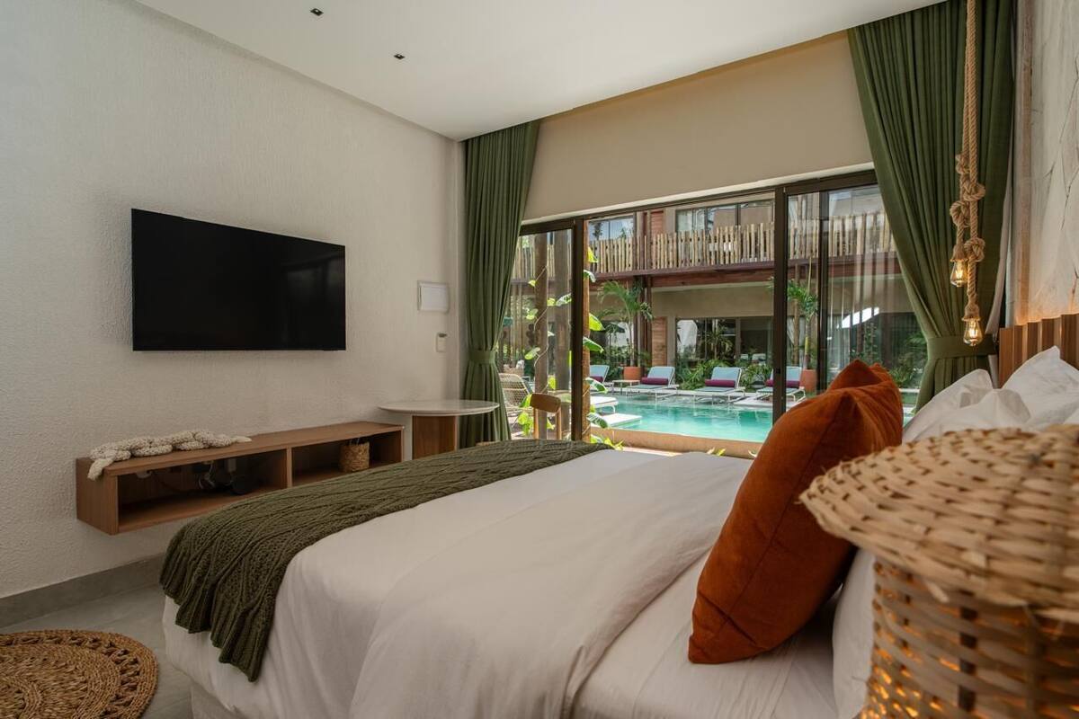 A bedroom with a large bed, a TV mounted on the wall, a small table, and a view of a pool and outdoor area.