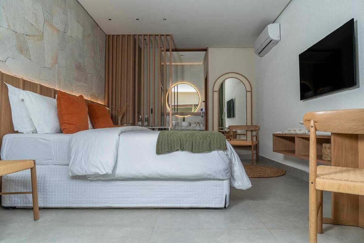 A modern bedroom with a large bed, a wooden headboard, a round mirror, and a TV mounted on the wall.