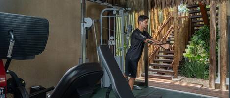 Un gimnasio con equipo de ejercicio, una escalera y vistas a un jardín tropical.