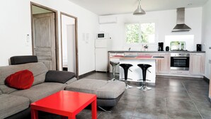 Una cocina moderna con una isla central, un comedor con mesa roja y un sofá gris con un cojín rojo.