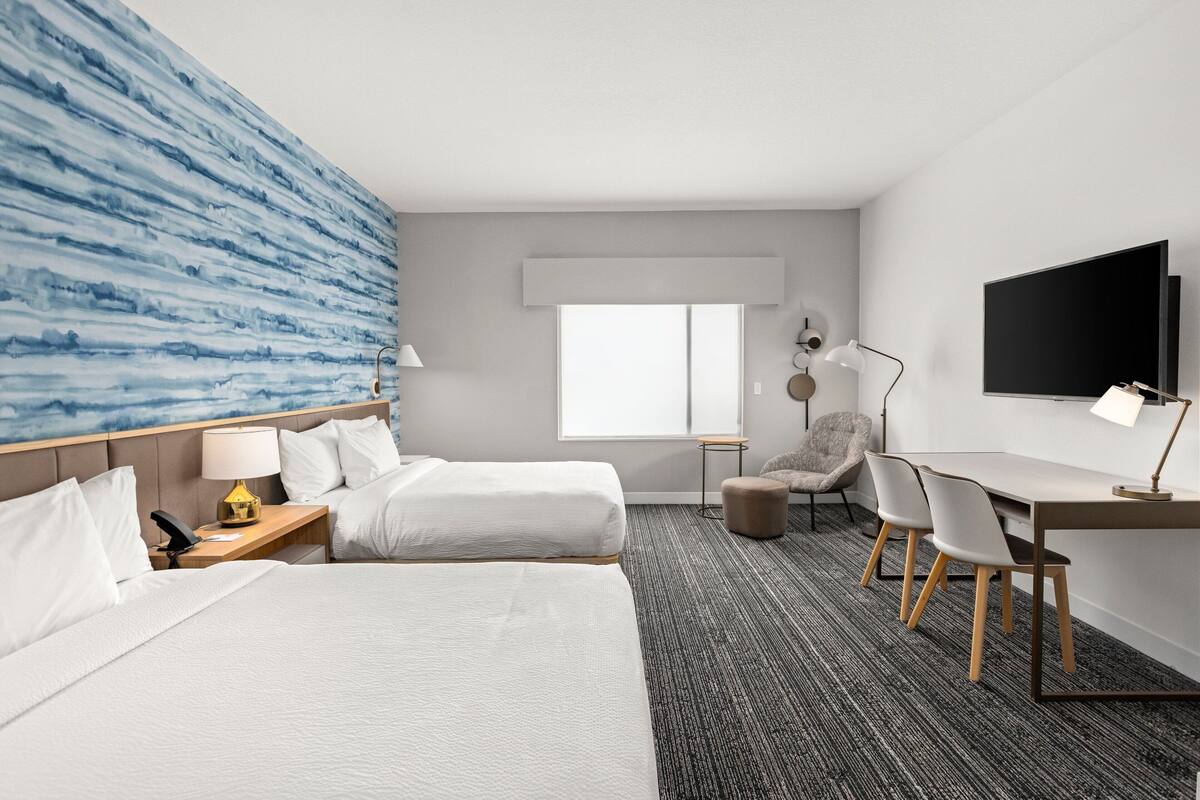 Ein Hotelzimmer mit zwei Betten, einem Schreibtisch, einem Stuhl, einem Fernseher und einem Fenster.