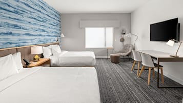 Ein Hotelzimmer mit zwei Betten, einem Schreibtisch, einem Stuhl, einem Fernseher und einem Fenster.
