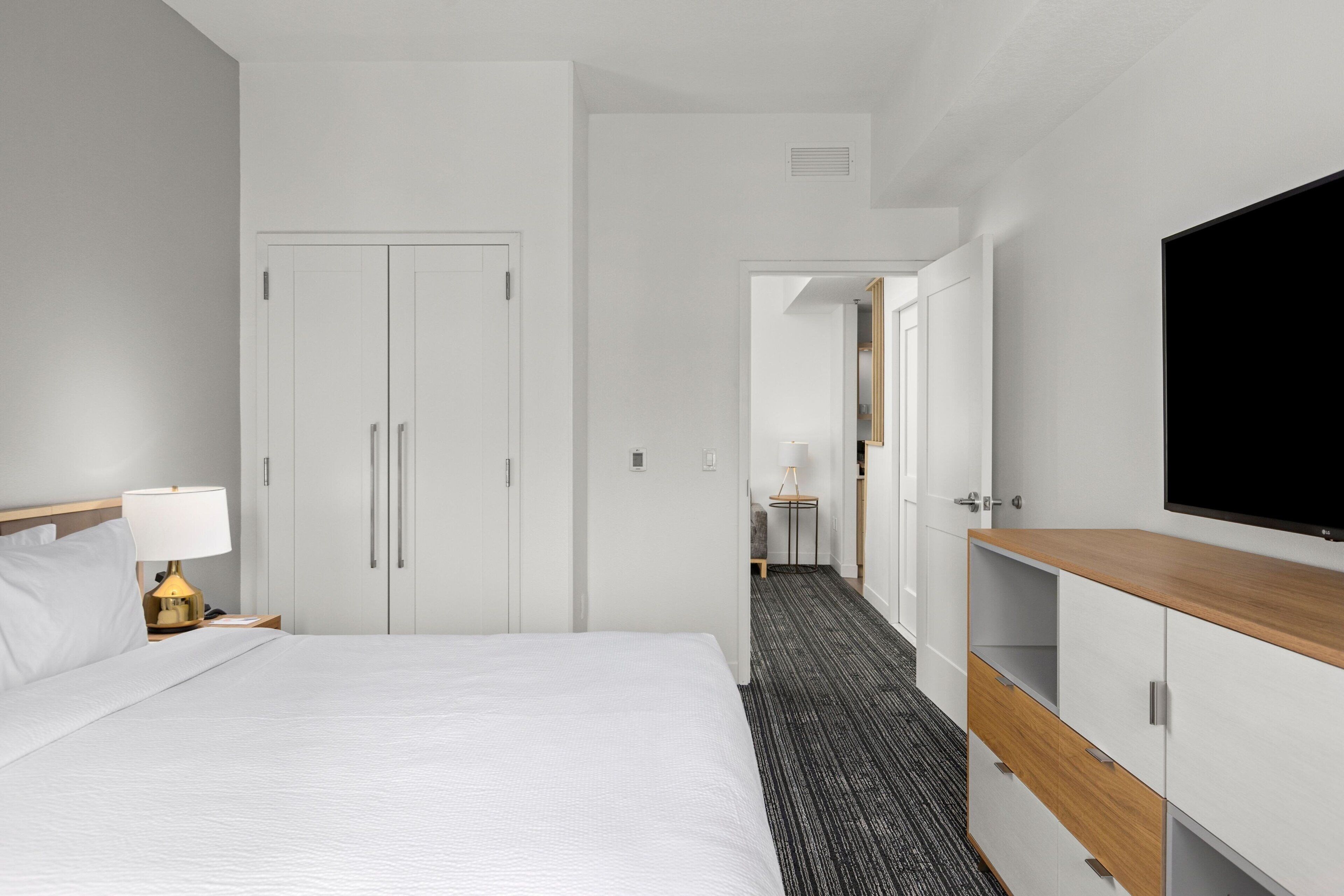A hotel room with a bed, a desk with a lamp, a TV, and a wardrobe.