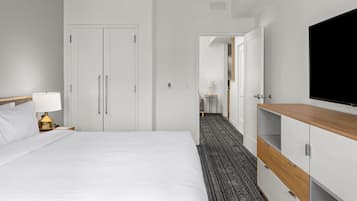 A hotel room with a bed, a desk with a lamp, a TV, and a wardrobe.