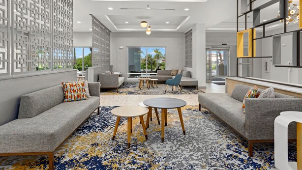A modern hotel lobby with grey sofas, round tables, and a patterned carpet.