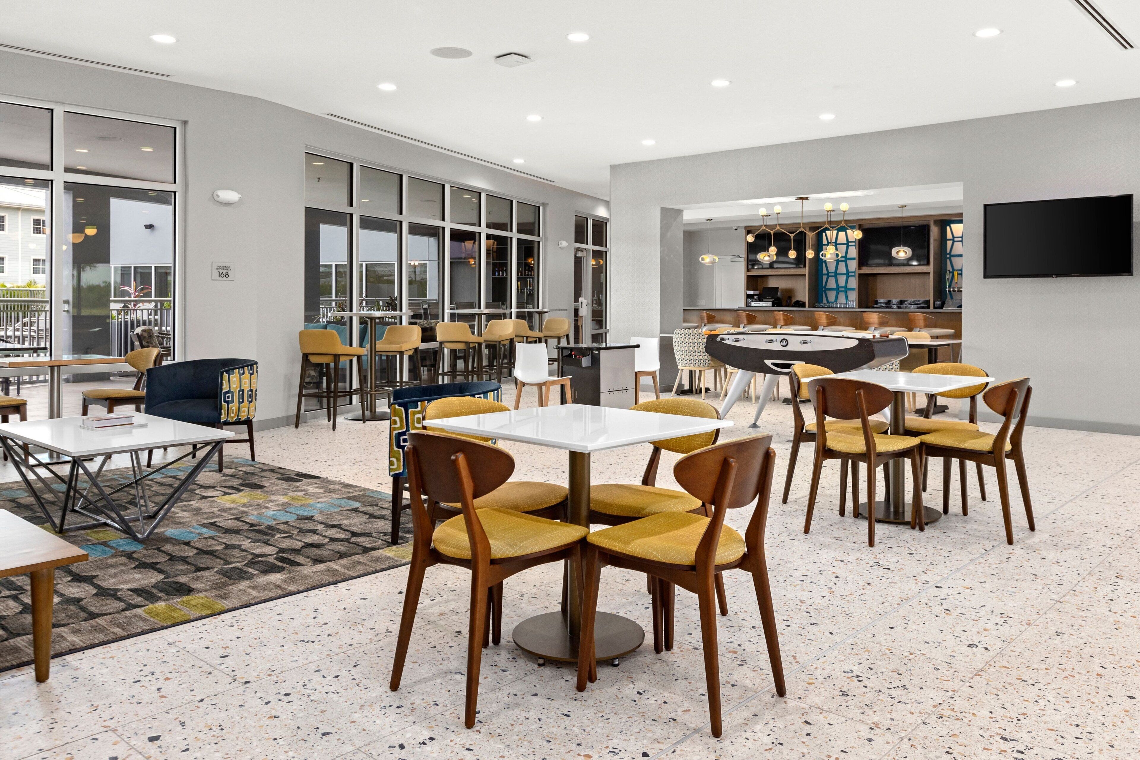 A modern dining area with multiple tables and chairs, large windows, and a bar area.