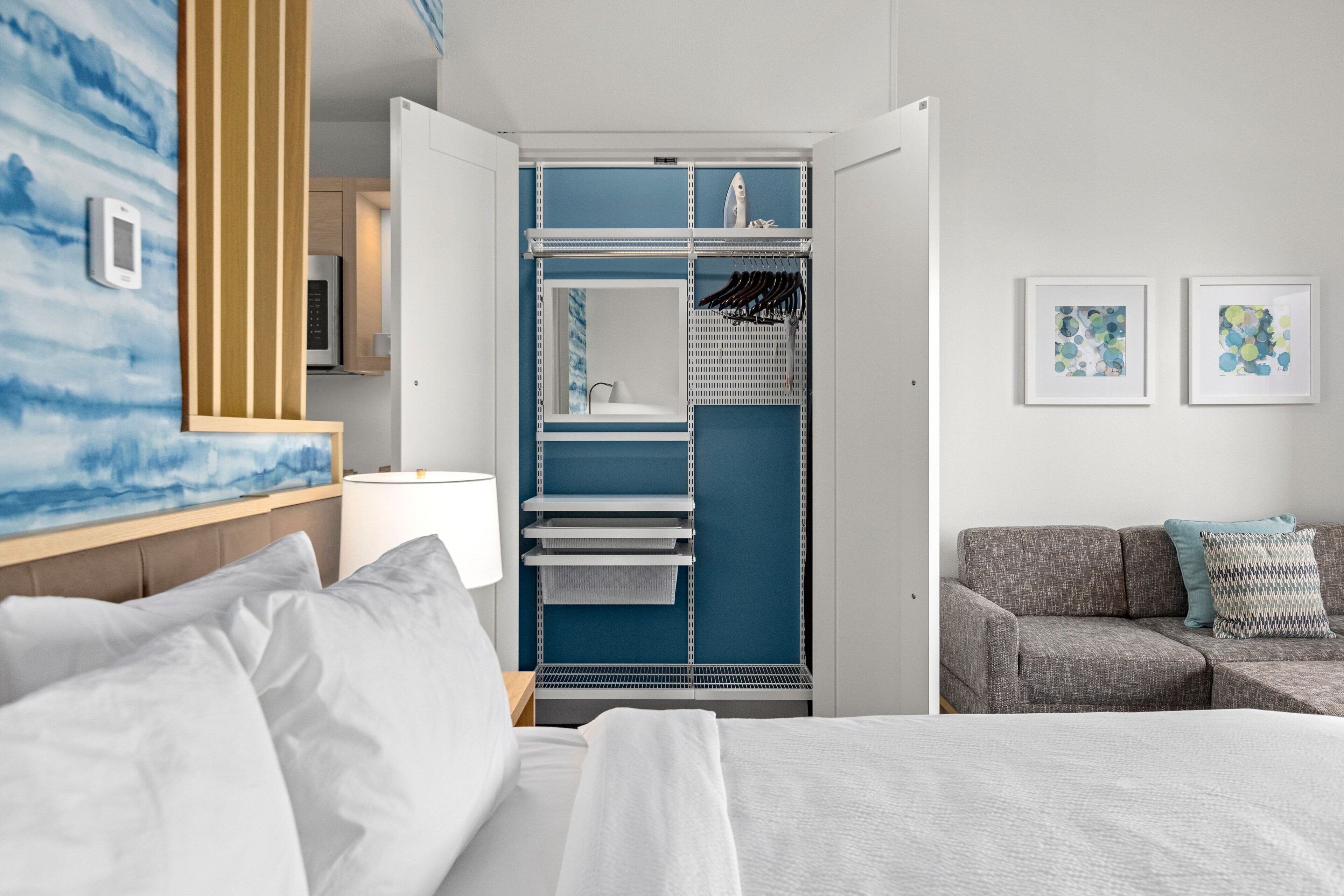 A hotel room with a bed, a sofa, a wardrobe with shelves, and a wall with a painting.