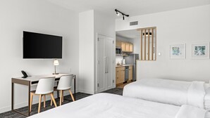 A hotel room with a bed, a desk with chairs, a television, and a kitchenette.