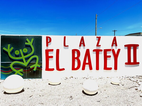 A sign for Plaza El Batey II with a colorful mural in the background.