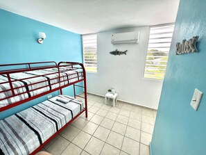 A room with a bunk bed, an air conditioner, a small table with a plant, and a window with blinds.