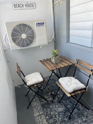 A small seating area with a table and two chairs, a potted plant, and an air conditioning unit labeled 'AIRMAX INVERTER' mounted on the wall.