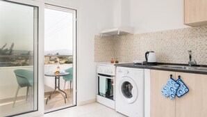 A kitchen with a washing machine, a coffee maker, and a view of the city through a sliding door. - Lungo Mare (Rhodes)