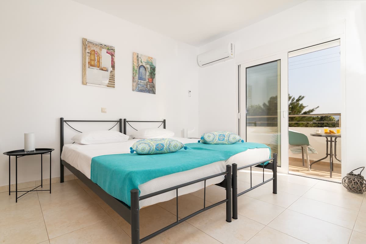 Ein Schlafzimmer mit Bett, einem kleinen Nachttisch, einem Balkon mit Tisch und Stühlen sowie zwei an der Wand befestigten Kunstwerken.