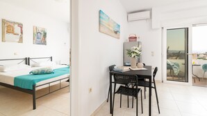 A modern hotel room with a bed, a dining table with chairs, a small table with a vase and books, and a balcony with a view. - Lungo Mare (Rhodes)