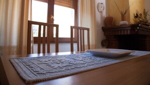 A dining table with a placemat, two wooden chairs, a white plate, and a vase with plants.