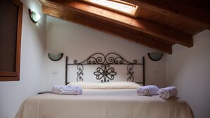 A neatly made bed with a decorative headboard, a skylight above, and a plain wall with a small window.