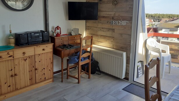 Una stanza con un armadio in legno, una scrivania con una sedia, un televisore fissato al muro e vista all'esterno tramite una porta in vetro.