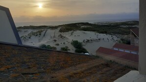 Vista di una spiaggia con dune sabbiose e un edificio con tetto rosso.