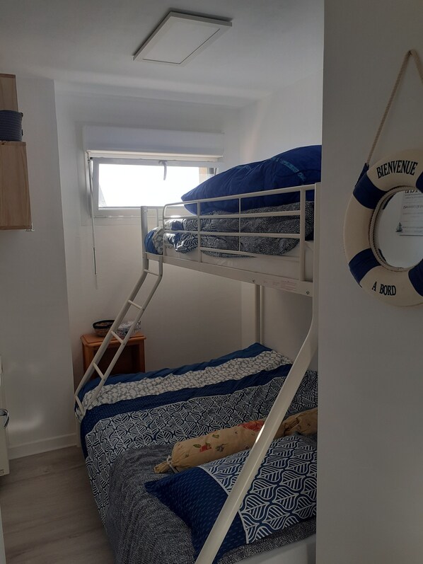 A bunk bed room with a window, a ladder, a small table, and a life preserver on the wall.