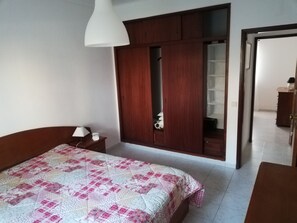 A bedroom with a bed, a nightstand, a wardrobe, and a door leading to another room.