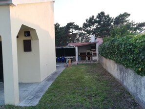 A courtyard with a white building, a small garden, and a covered area with blue chairs.