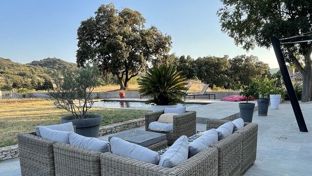 A wicker sofa with cushions, a small table, and potted plants in an outdoor patio area with a view of trees and hills. - Magnifique Villa D'architecte A 10 Minutes D'avignon (Tavel)