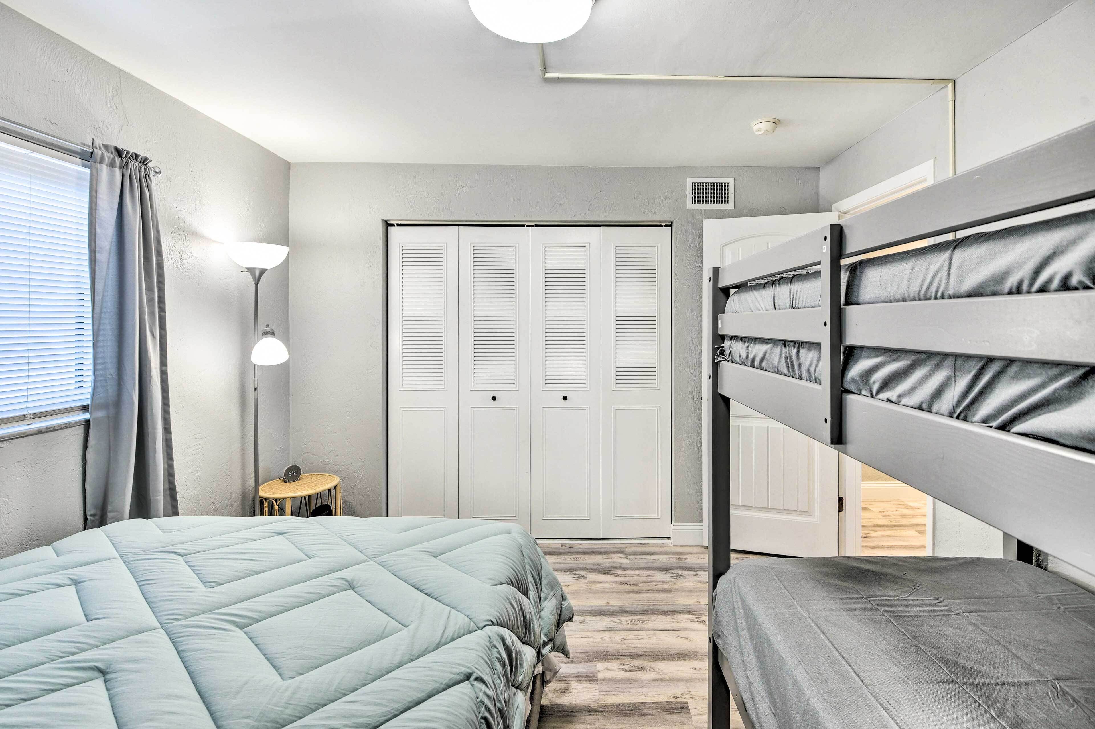 A bedroom with a bunk bed, a single bed, a bedside table, a lamp, and a closet.