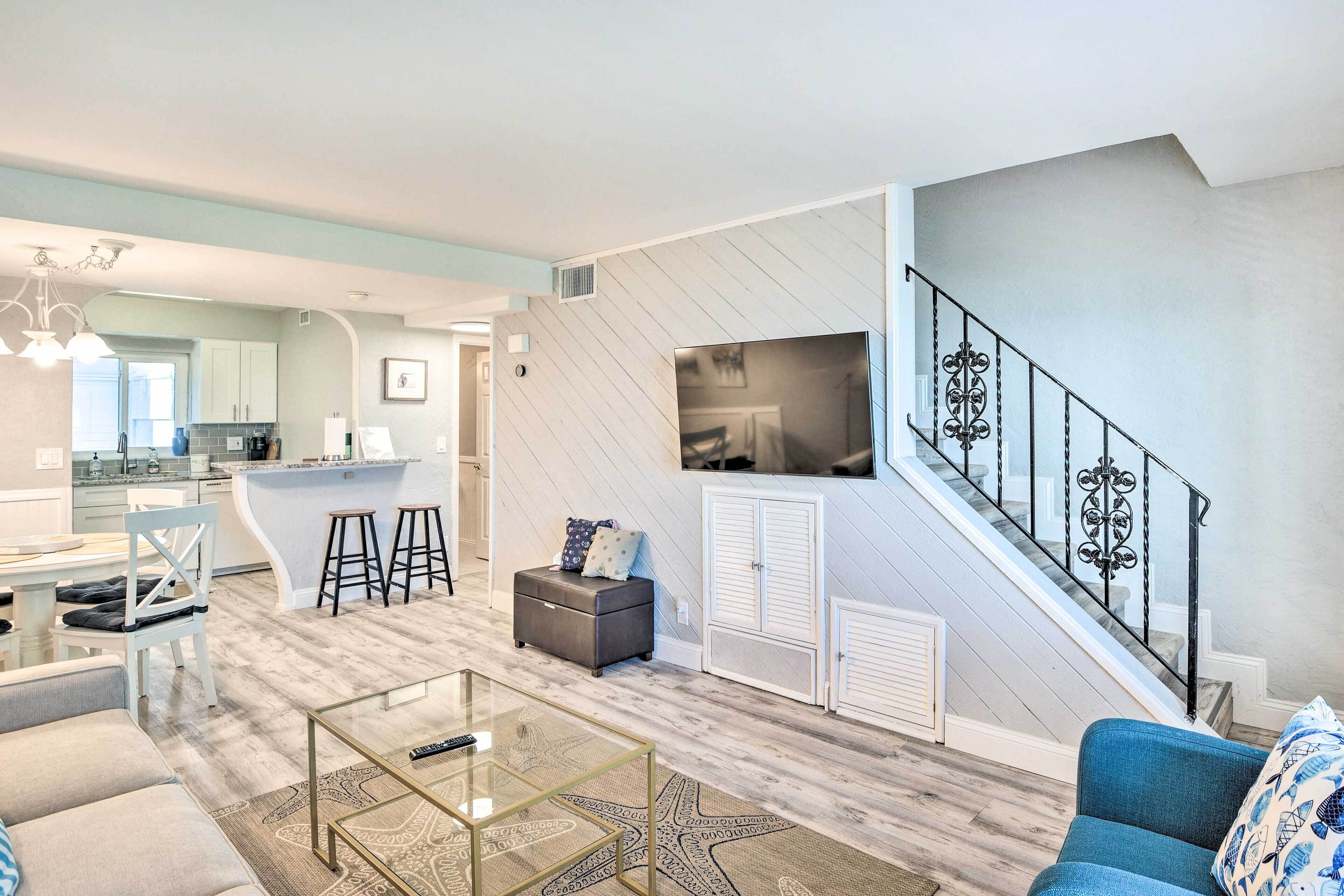 Un saló modern amb una taula de centre de vidre, un sofà blau i una escala amb barana decorativa.