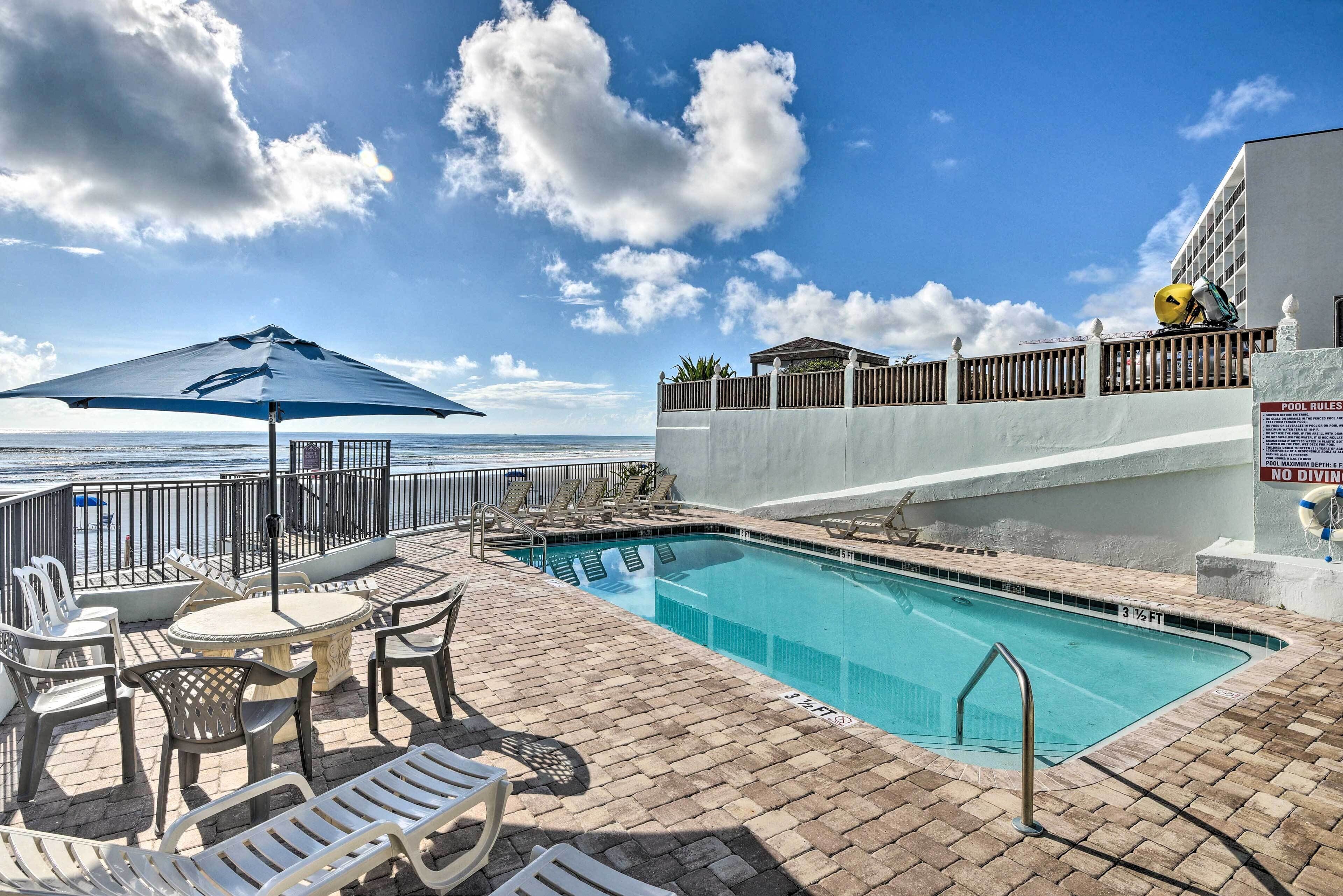 Ein Poolbereich mit Liegestühlen, einem Tisch und Blick auf das Meer.