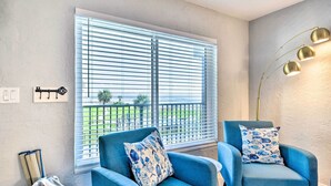 A room with a large window, two blue armchairs with patterned cushions, a floor lamp, and a view of a green landscape. - Airy Oceanfront Condo: Steps to Daytona Beach (Daytona Beach)