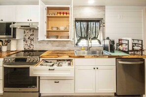 A modern kitchen with white cabinets, a wooden countertop, an LG stove, a dishwasher, and a window with curtains.