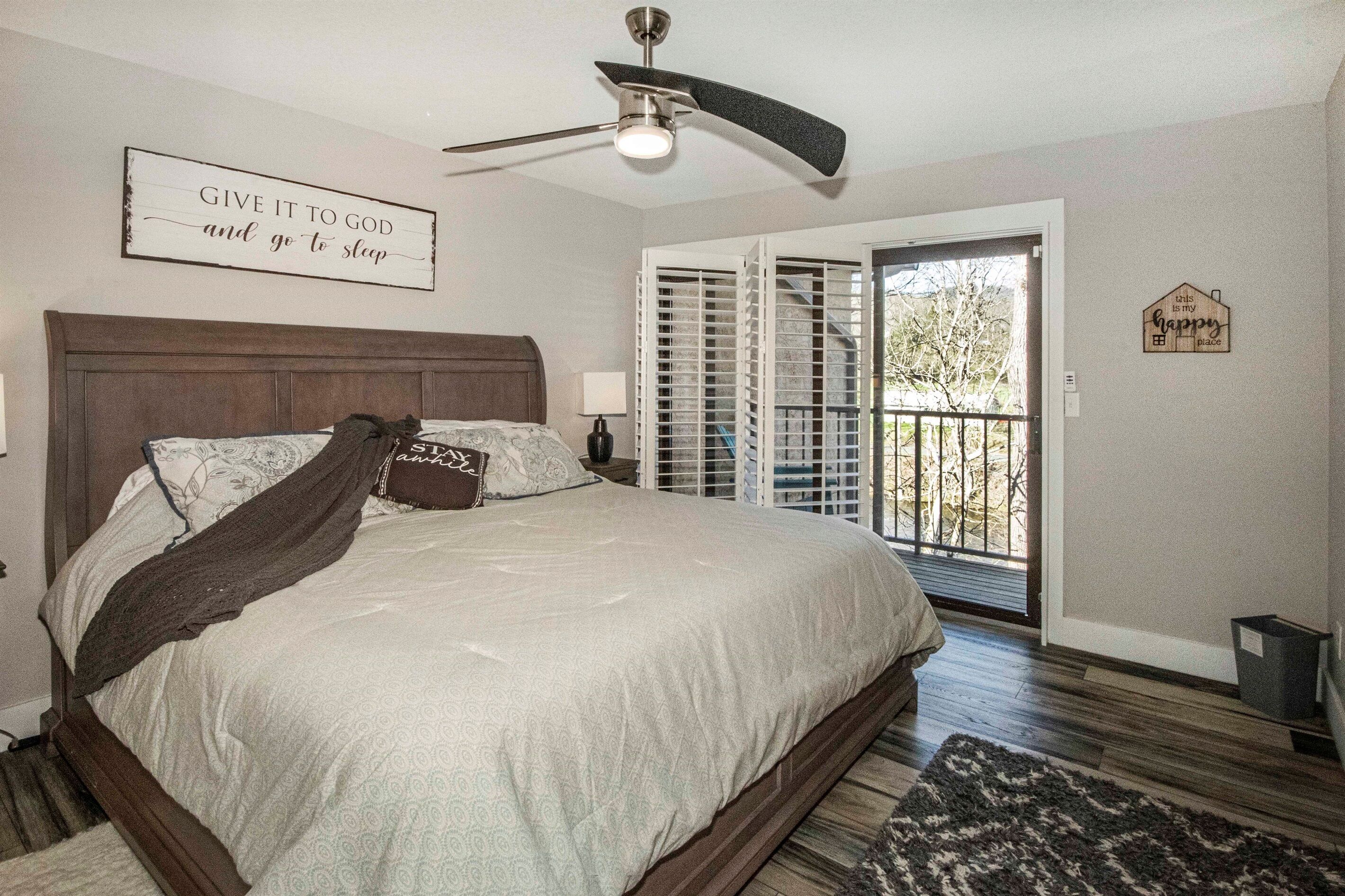 A bedroom with a bed, a ceiling fan, a window with blinds, and a door leading to a balcony.