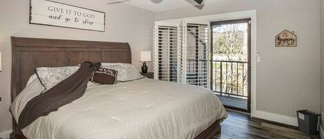 A bedroom with a bed, a ceiling fan, a window with blinds, and a door leading to a balcony.