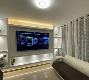 A modern living room with a flat-screen TV mounted on the wall, a white sofa, and a decorative plant.