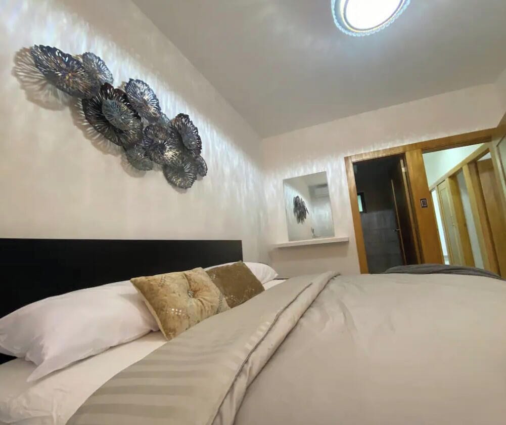 A bedroom with a bed, a wall-mounted decorative piece, and a door leading to another room.