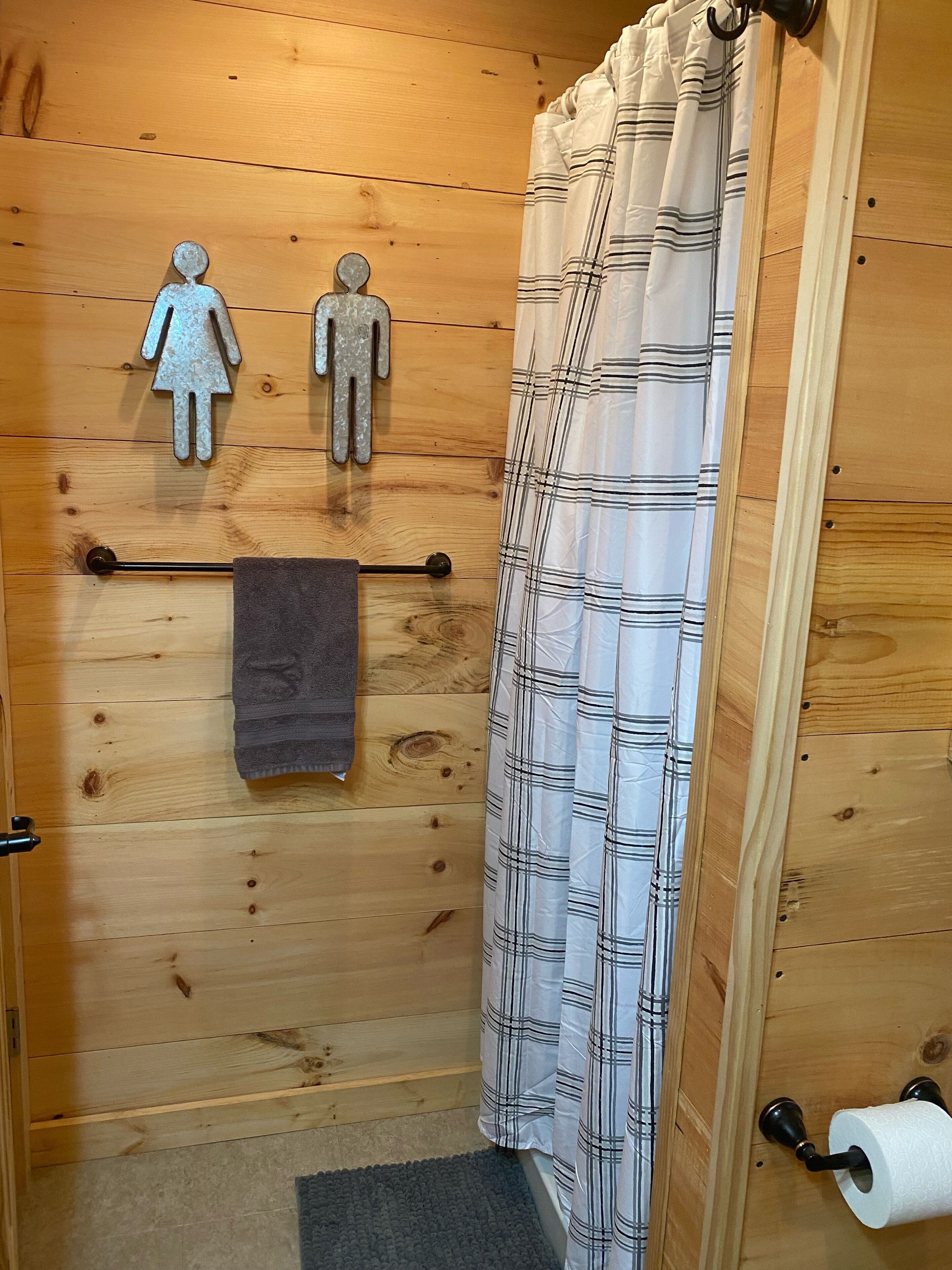 Een houten badkamer met douchegordijn, een handdoekrek met een handdoek, en twee toiletrolhouders aan de muur.