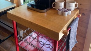 Una mesa de madera con una cafetera Keurig, dos tazas blancas y una cesta pequeña.