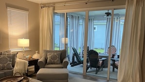 Een ruime woonkamer met een plafondventilator, een zithoek, een salontafel en uitzicht door grote schuifdeuren op een terras.