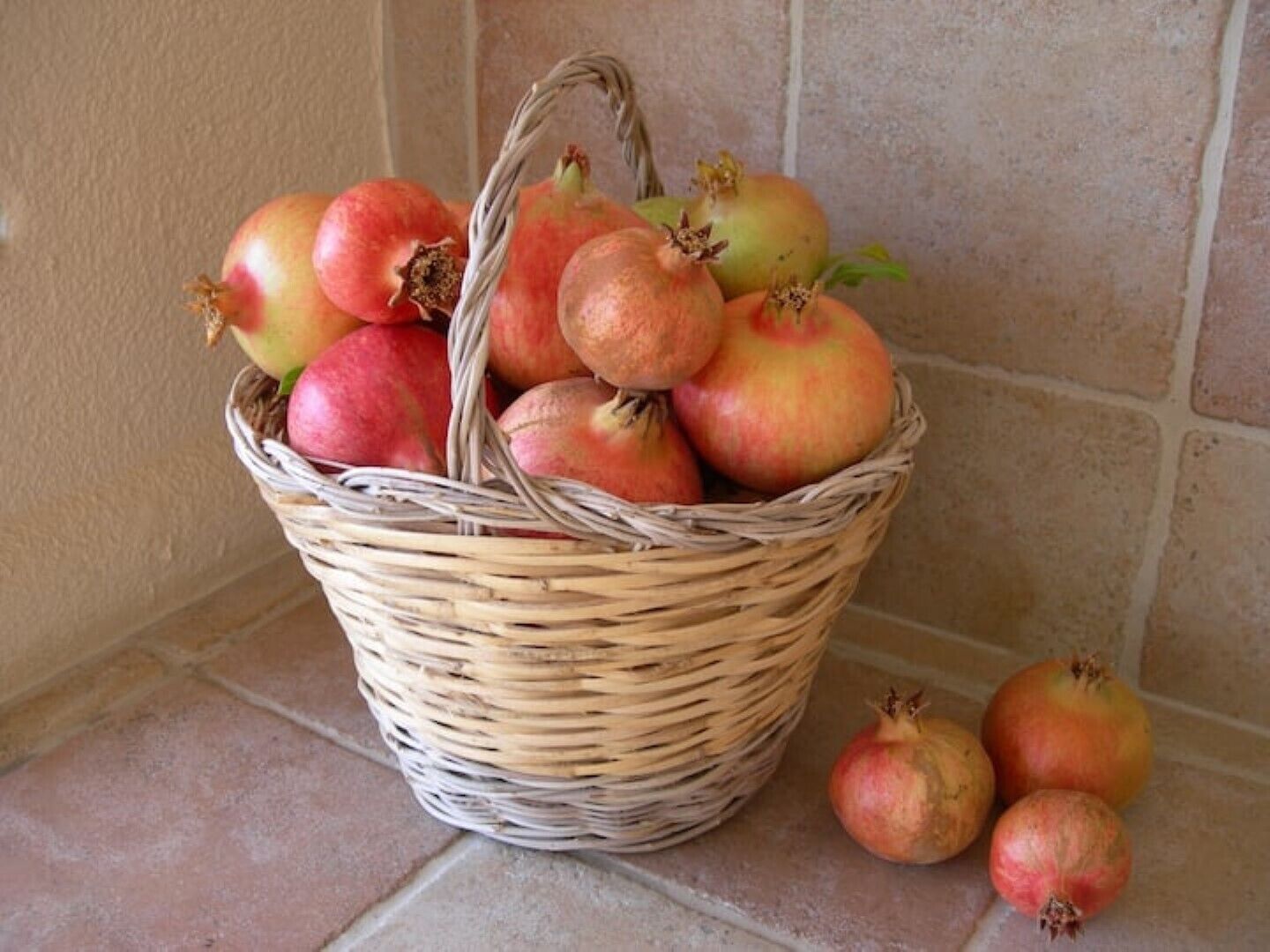 Een rieten mand vol granaatappels op een betegelde vloer.