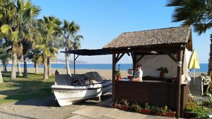 A beachside kiosk with a thatched roof, a wooden dock, and a boat named 'CASA MIGUEL' parked nearby.